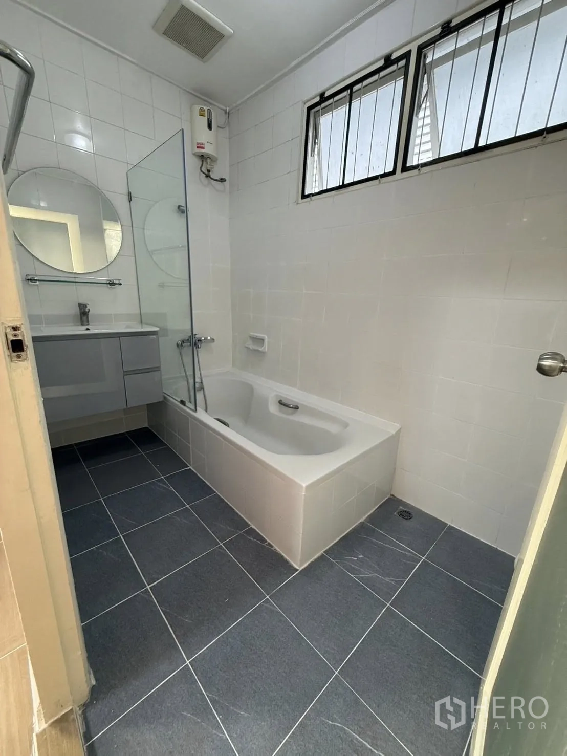 Detached House for rent in Khlong Toei, Bangkok - Bathroom featuring a bathtub, vanity, wall-mounted water heater, and window.