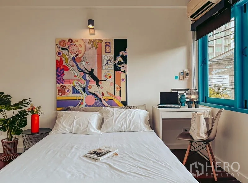 Home Office for rent in Watthana, Bangkok - Bedroom with white bed, colorful artwork, desk by the window, and blue trim.