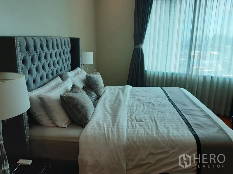 Condominium for rent or sale in Khlong Toei, Bangkok - Primary bedroom with tufted headboard, bedside lamps and a large window with curtains.