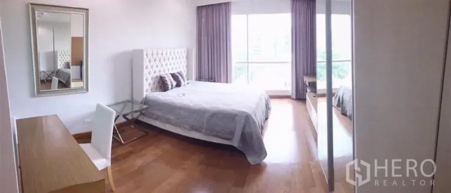 Condominium for rent in Pathum Wan, Bangkok - Spacious bedroom with king bed, tufted headboard, desk, mirrored wardrobe and a large window with curtains.