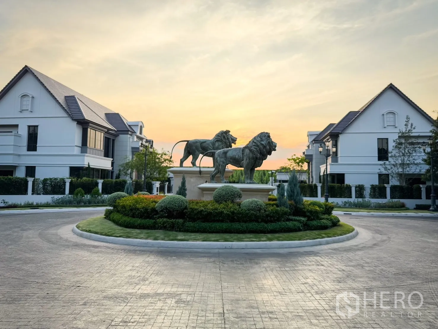 Detached House for rent in Bang Khen, Bangkok - Community roundabout featuring lion statues surrounded by luxury homes at sunset.