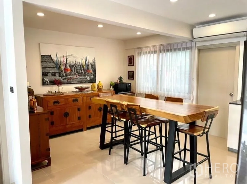 Townhouse for rent in Suan Luang, Bangkok - Dining corner featuring a wood buffet cabinet, artwork, and large windows.