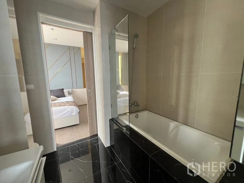 Condominium for sale - Modern bathroom with bathtub, glass screen and black marble floor.