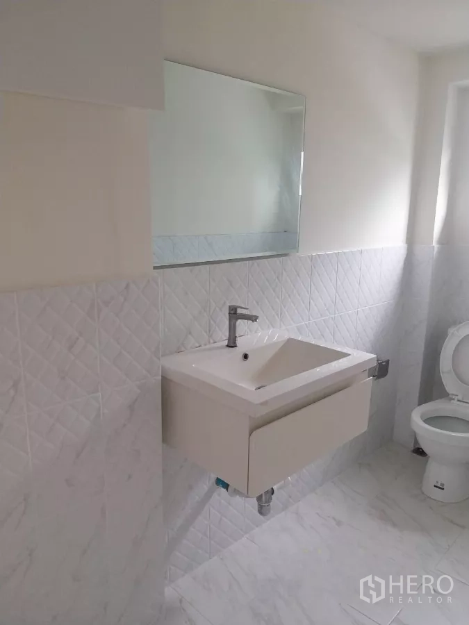 Retail Space for rent - Clean white-tiled bathroom with wall mirror, basin and toilet inside the retail unit.