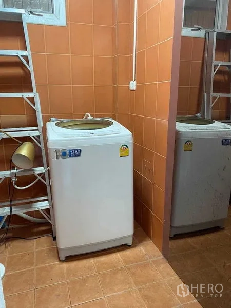 Home Office for rent in Khlong Toei, Bangkok - Laundry room with top-loading washing machines and orange wall tiles.