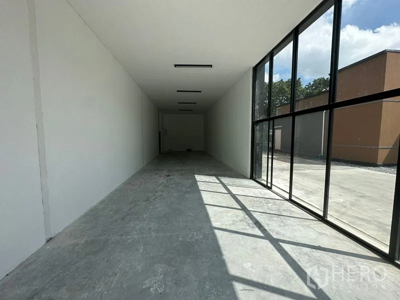 Warehouse for rent in Bang Phli, Samut Prakan - Bright front showroom or office with floor-to-ceiling black-frame glass wall and grey floor.