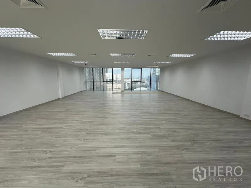 Office Space for rent - Wide open workspace with uniform ceiling lights and full-height windows facing the city