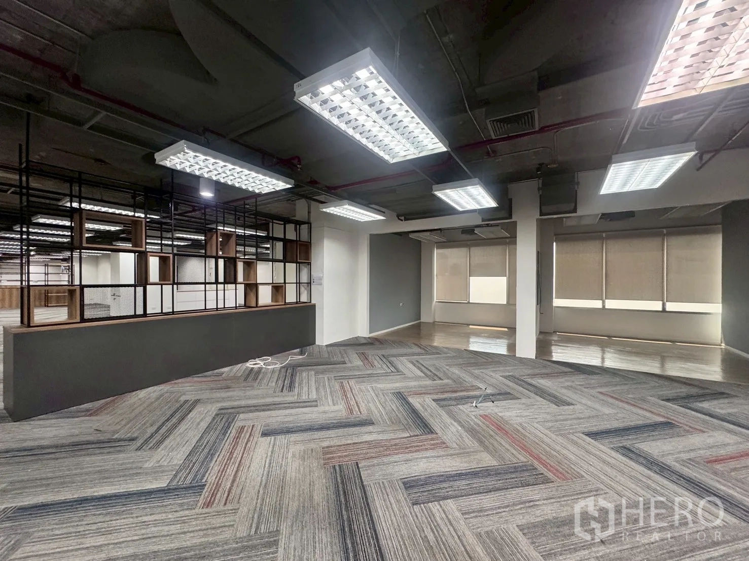 Office Space for rent in Watthana, Bangkok - Collaborative space with a black grid shelving divider and an adjacent wood-floored area with blinds.