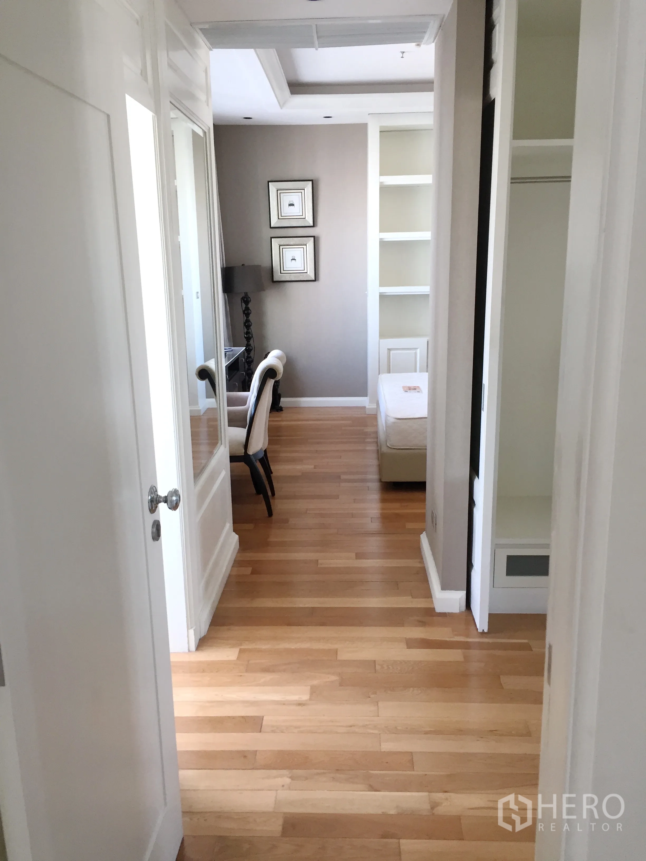 Condominium for rent in Khlong Toei, Bangkok - Light hallway with hardwood flooring leading to a bedroom with built-in shelving and neutral decor.
