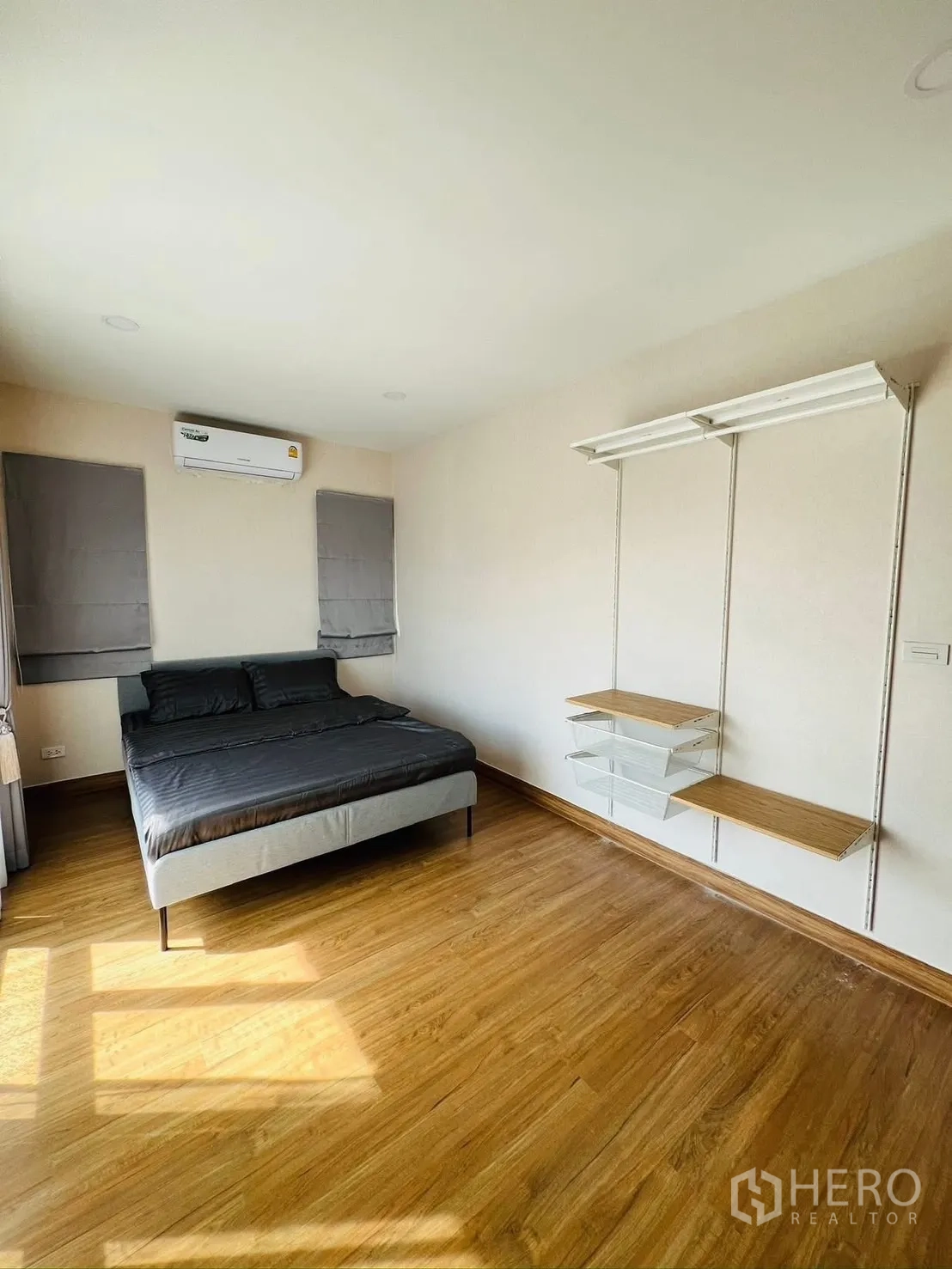 Detached House for rent in Prawet, Bangkok - Spacious bedroom with air conditioner, bed and wall-mounted shelving over wood flooring.