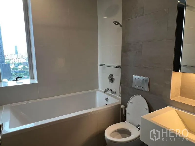 Condominium for rent - Contemporary bathroom with bathtub, toilet and vanity plus a window framing the city view.