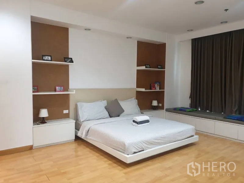 Condominium for rent in Khlong Toei, Bangkok - Master bedroom with wall shelves and long window bench under dark curtains.
