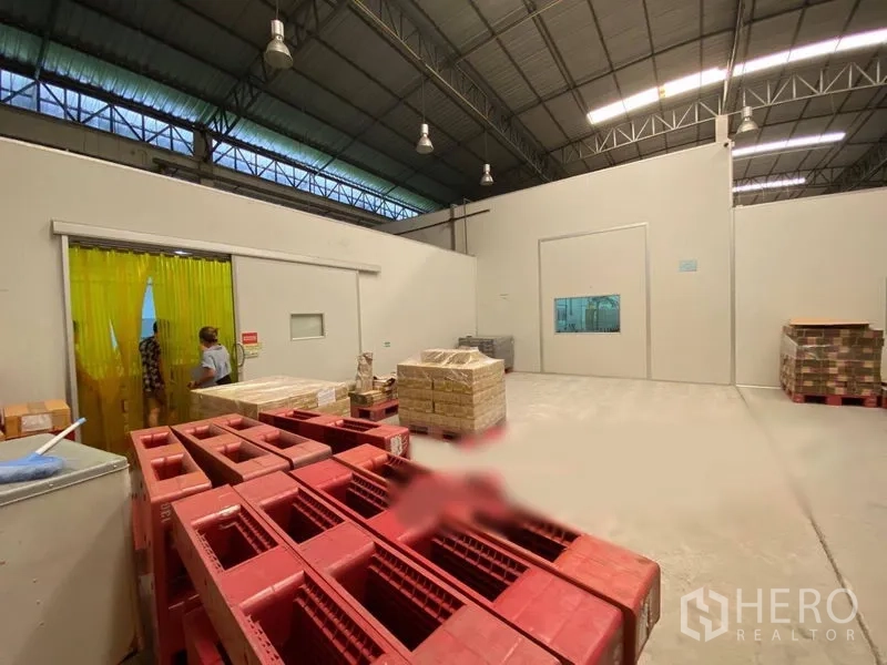 Warehouse for rent in Bueng Kum, Bangkok - Warehouse corner with yellow strip curtains, partitioned rooms, and stacked plastic crates.