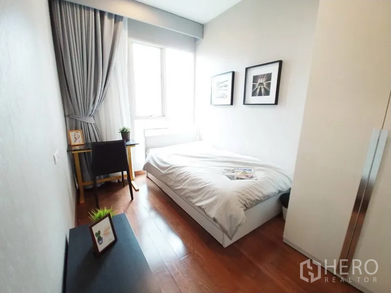 Condominium for rent in Pathum Wan, Bangkok - Cozy second bedroom with window, study desk, grey curtains and framed artwork.