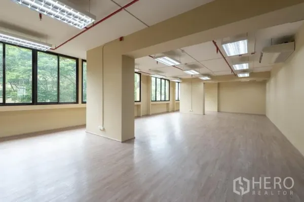 Office Space for rent in Chatuchak, Bangkok - Spacious open-plan office with wood-look flooring, bright fluorescent lighting, and large windows facing greenery.