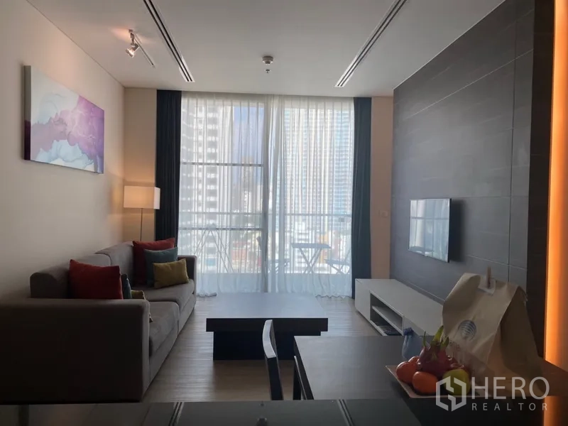 房间 出租在Khlong Toei, Bangkok - Nana区公寓明亮客厅，配沙发、茶几、壁挂电视与城市景观阳台。