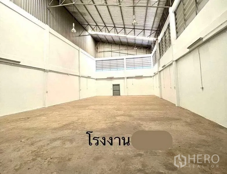 Factory for rent or sale in Mueang Samut Sakhon, Samut Sakhon - Spacious warehouse hall with high steel truss ceiling, white walls and concrete floor.