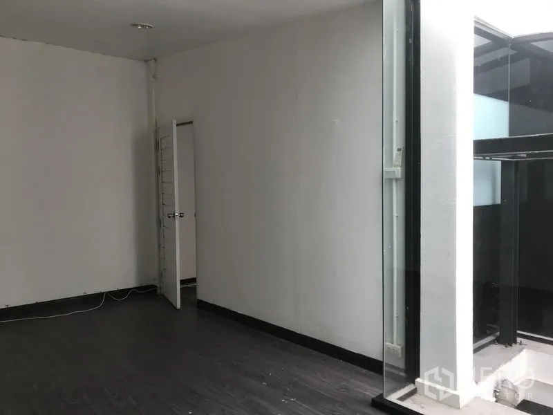 Shophouse for rent in Watthana, Bangkok - Bright room opening to an internal glass lightwell with dark flooring and white walls.