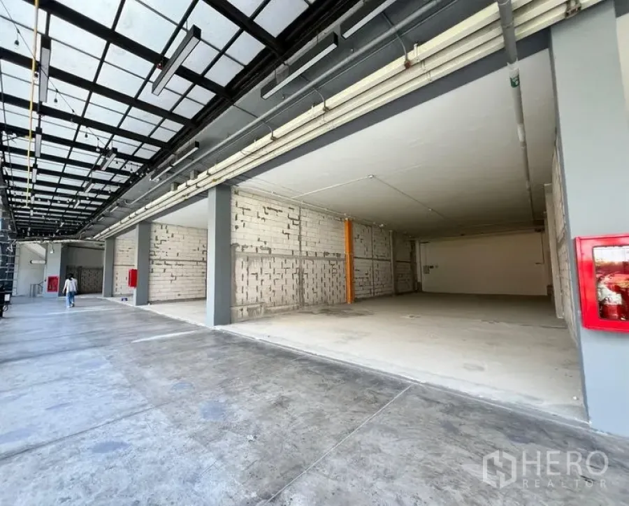 Retail Space for rent - Wide shopfront bay opening to a covered arcade with high canopy, unfinished interior and visible fire safety fixtures.