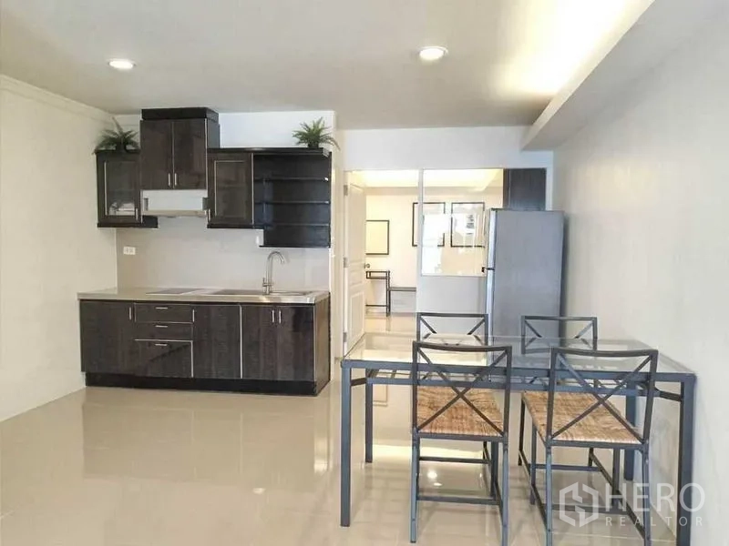 Condominium for rent in Khlong Toei, Bangkok - Compact kitchen with dark cabinetry, sink and a glass-top dining table in a minimalist Bangkok apartment.