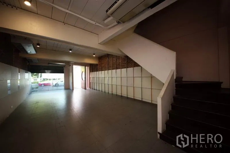 Home Office for rent or sale in Huai Khwang, Bangkok - Open-plan ground floor with staircase, ceiling spotlights and large storefront window.