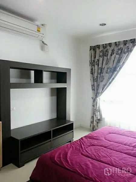 Condominium for rent in Khlong Toei, Bangkok - Bedroom with media cabinet, air conditioner and floral drapes by the window.