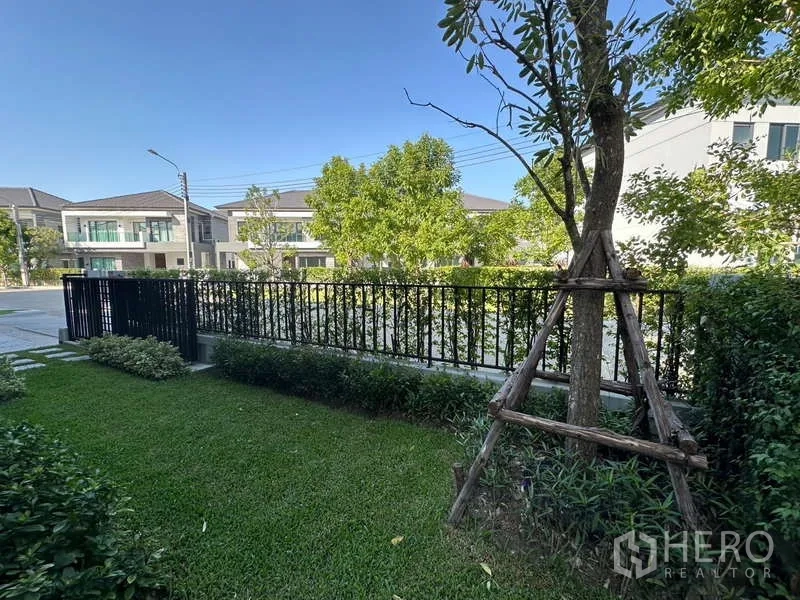 Detached House for rent in Bang Phli, Samut Prakan - Landscaped front garden with lawn, trees and a black metal fence inside the estate.