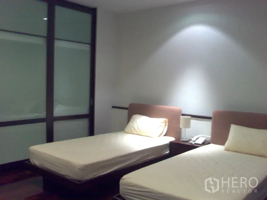 Condominium for rent in Watthana, Bangkok - Twin-bed bedroom with soft lighting, wood floors and frosted sliding glass wardrobe doors.