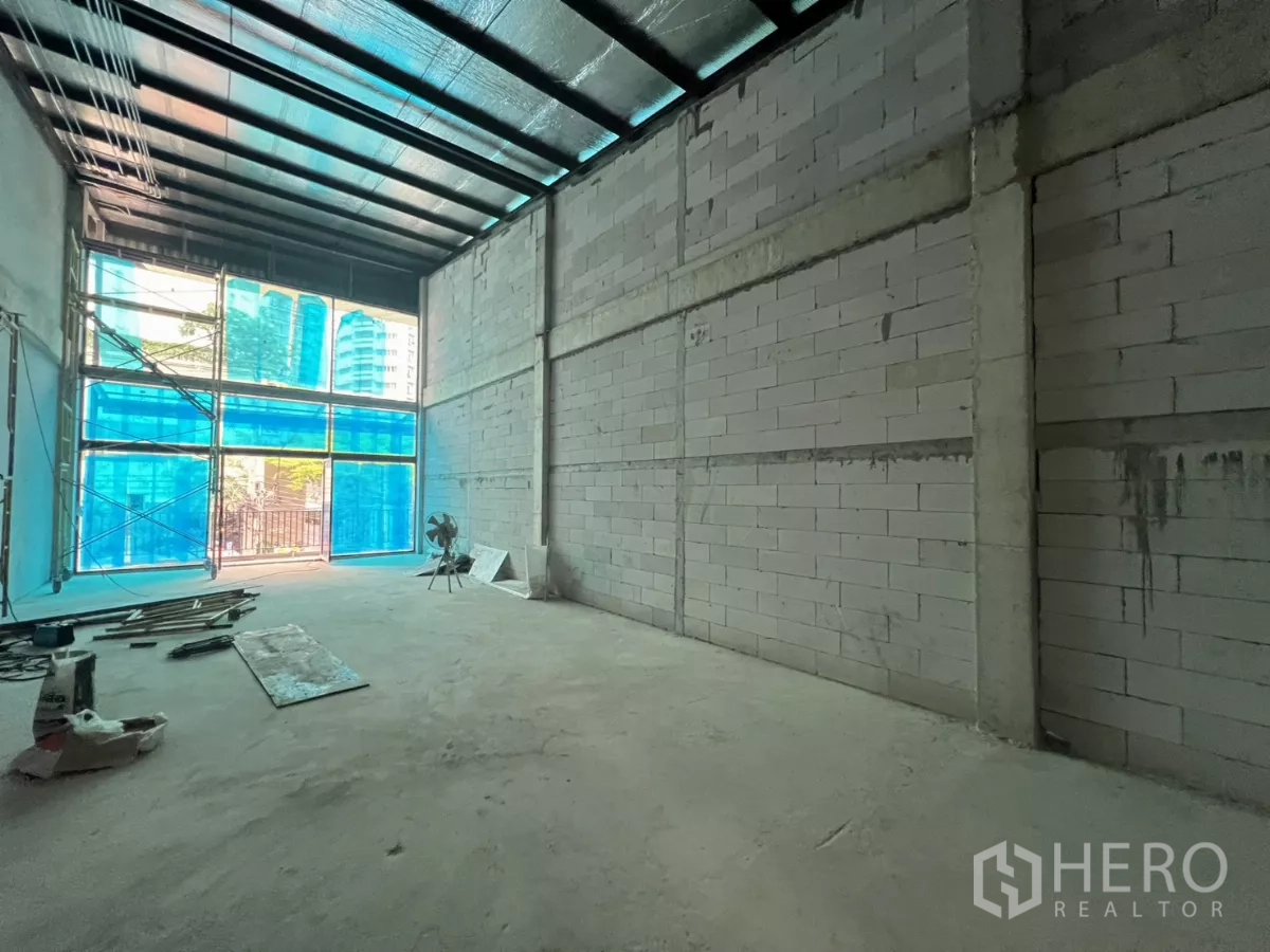 Retail Space for rent in Khlong Toei, Bangkok - Double-height shell retail space with exposed ceiling and blue window coverings.