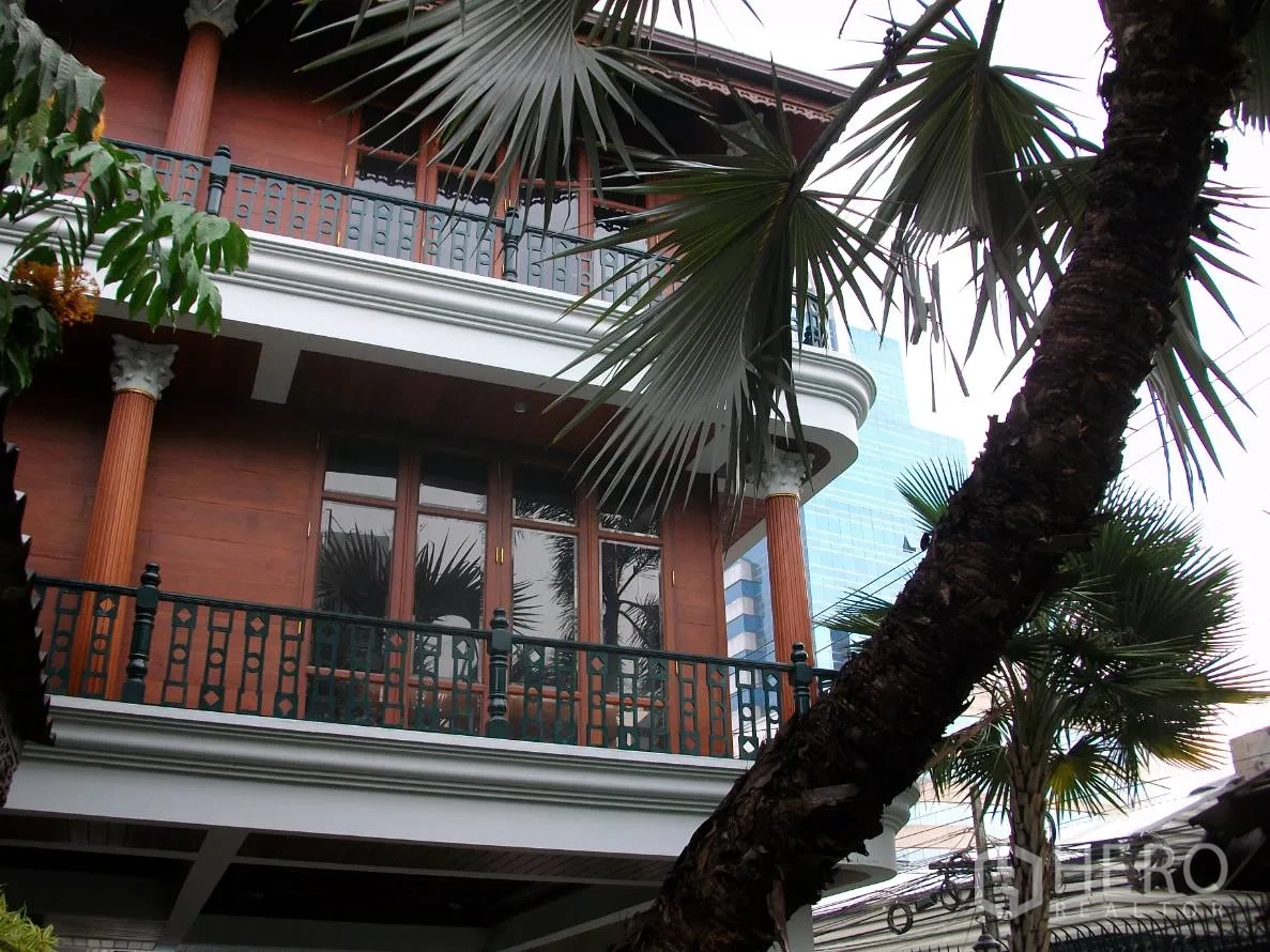 Detached House for rent in Khlong Toei, Bangkok - Two-storey Thai-style house facade with balcony, columns and tall palm trees.