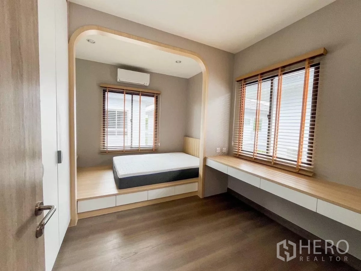 Detached House for rent or sale in Prawet, Bangkok - Cozy bedroom with platform bed nook, big windows with wooden blinds and a long built-in desk.