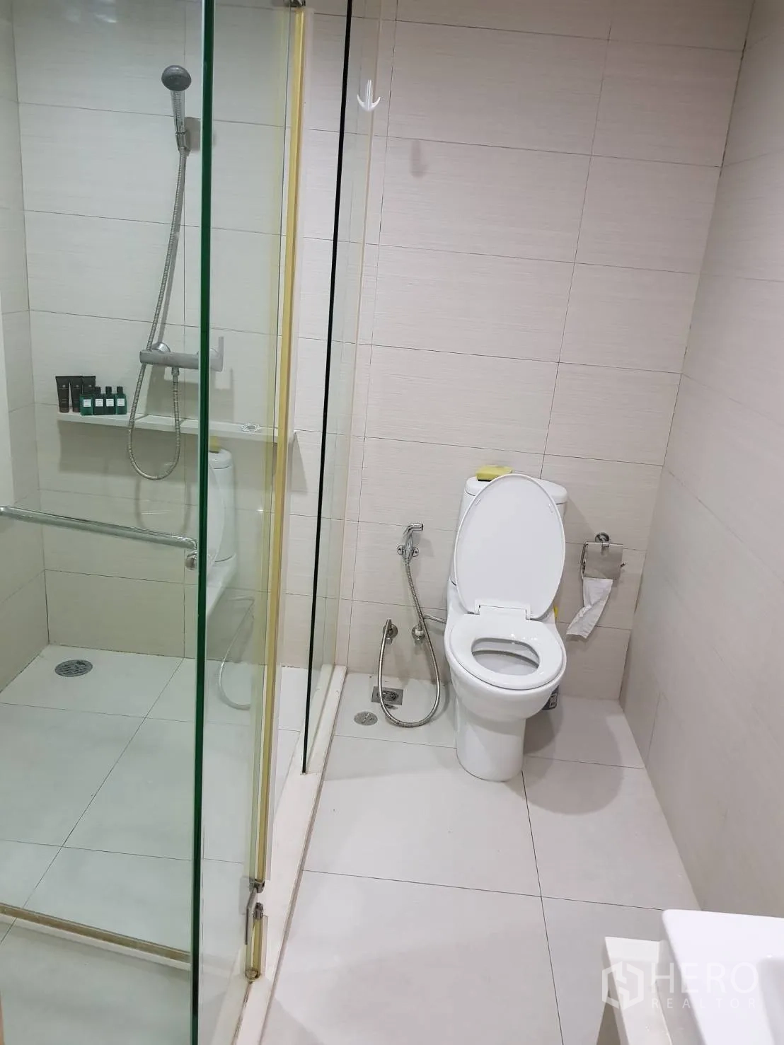 Condominium for rent in Khlong Toei, Bangkok - Bright bathroom with glass-enclosed shower, handheld showerhead and modern toilet.