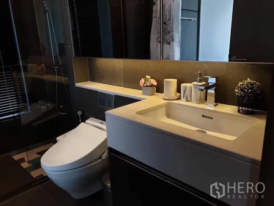 Condominium for rent in Huai Khwang, Bangkok - Modern bathroom with sleek vanity, toilet, and a glass-enclosed shower.