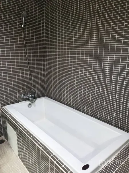 Condominium for rent in Khlong Toei, Bangkok - Tiled bathroom with rectangular bathtub and handheld shower.