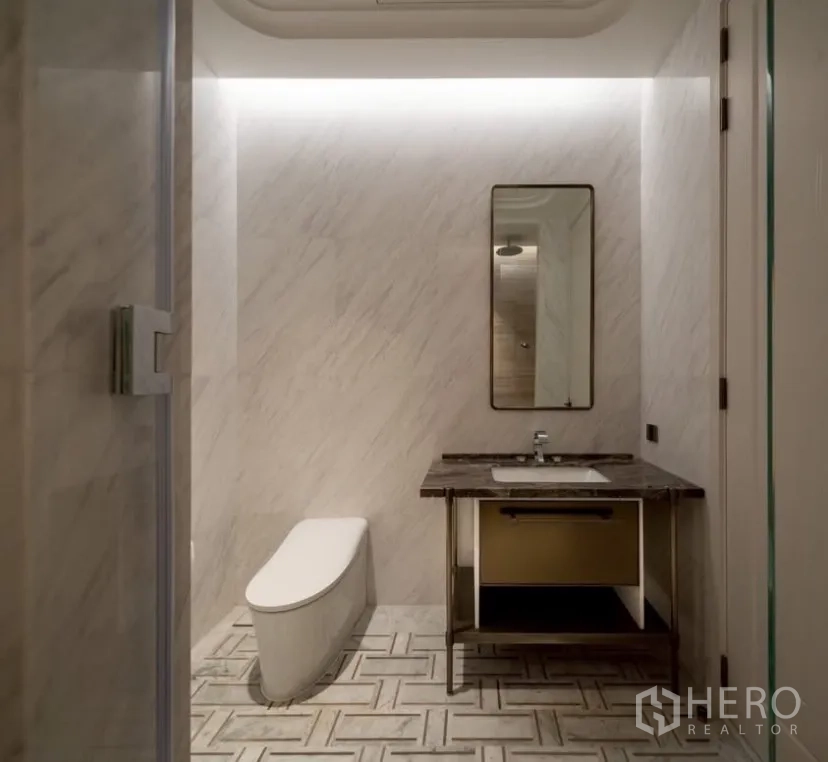 Condominium for rent or sale in Pathum Wan, Bangkok - Contemporary bathroom with floating vanity, sleek toilet and marble-tile walls.