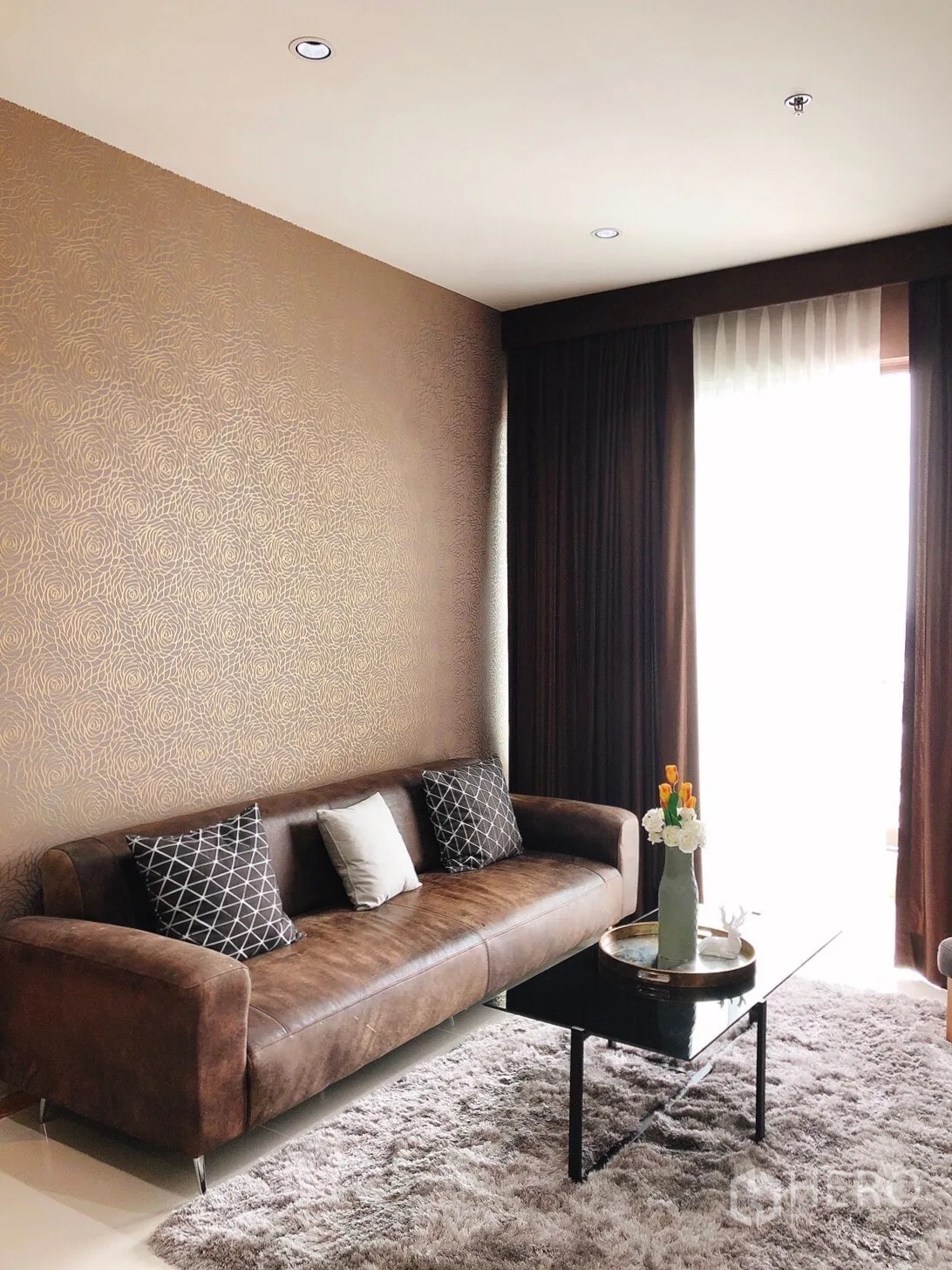 Condominium for rent in Khlong Toei, Bangkok - Close-up of living area with brown sofa, patterned cushions and glass coffee table.