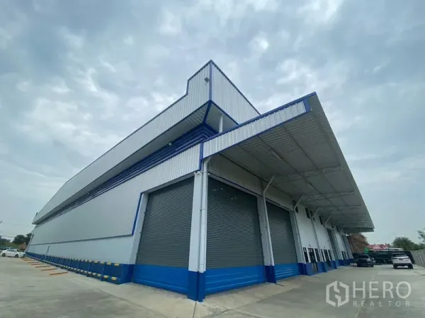 货栈 出租在Pathum Thani - 新仓库转角外观，多个卷帘门与大型雨棚装卸区。