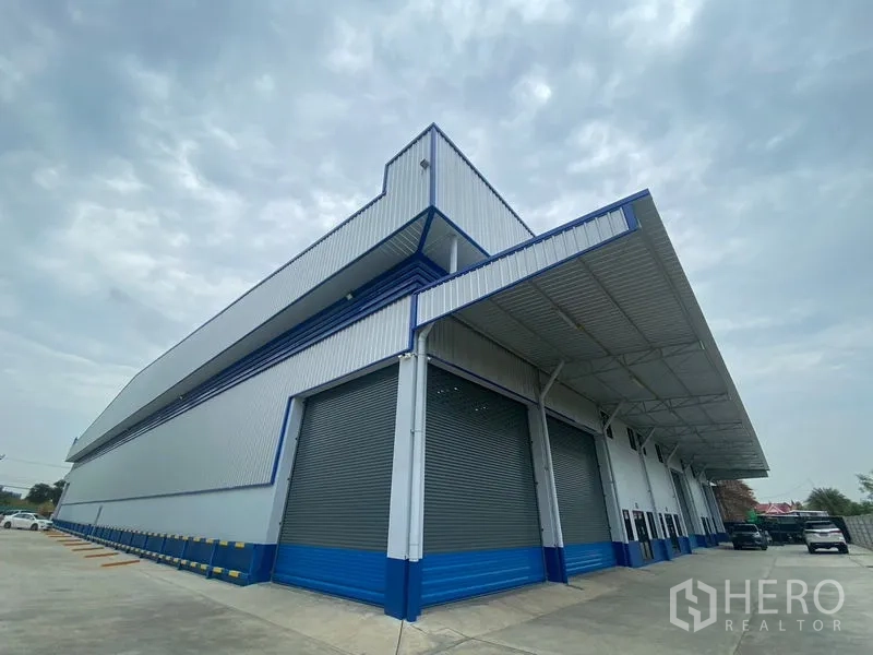 货栈 出租在Pathum Thani - 新仓库转角外观，多个卷帘门与大型雨棚装卸区。