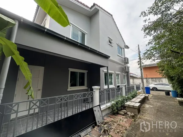 Townhouse for sale in Lam Luk Ka, Pathum Thani - Side walkway beside the house with garden benches and shrubs.