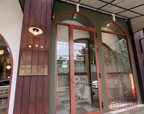 零售空间 出租在Watthana, Bangkok - 拱形玻璃入口，木质边框与外墙壁灯。