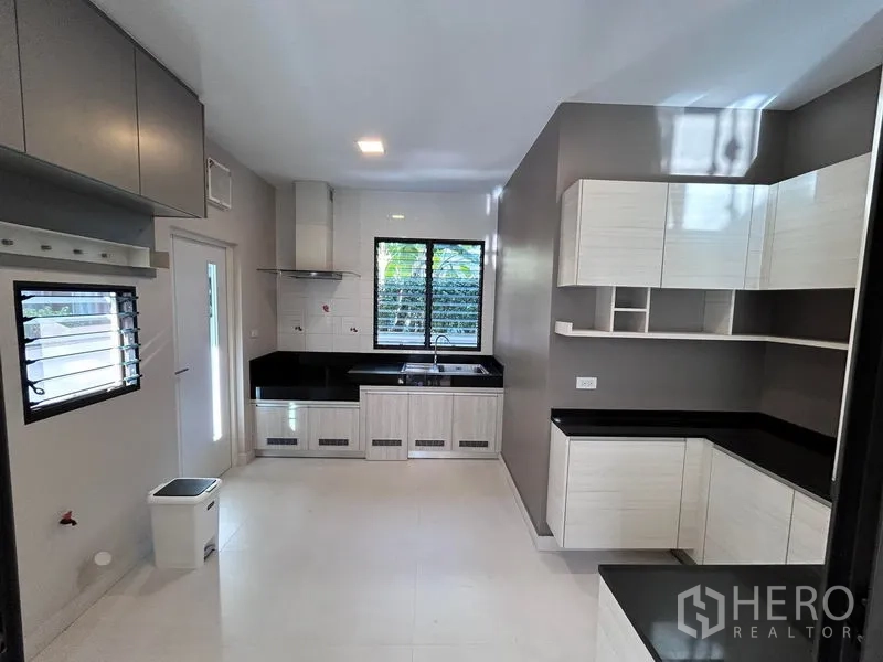 Detached House for rent or sale in Prawet, Bangkok - Spacious kitchen with black countertops, white cabinetry, and a window.