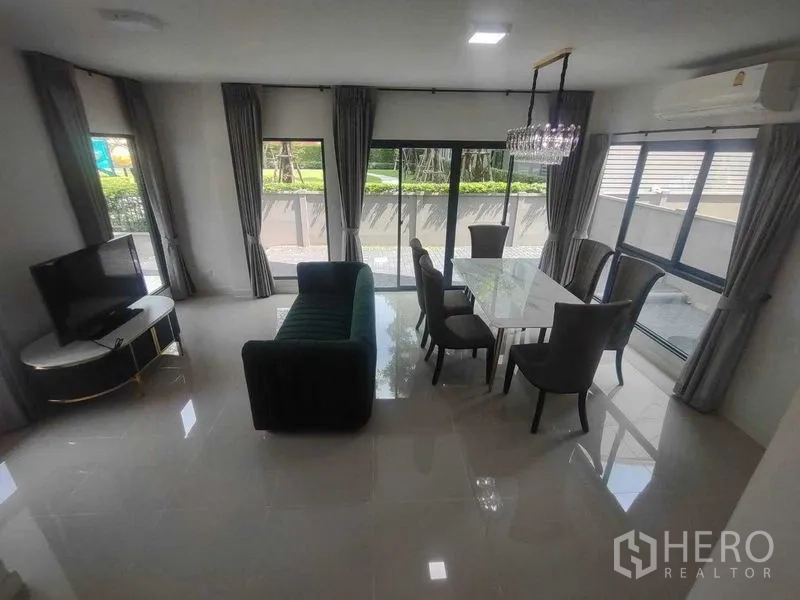 Detached House for rent in Khan Na Yao, Bangkok - Open‑plan living and dining room with sofa, TV and full‑height windows.
