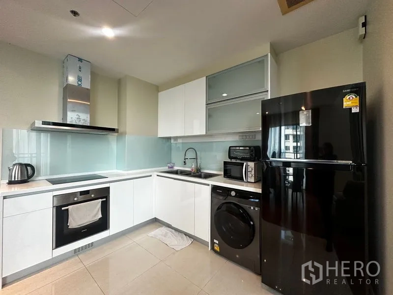 Condominium for rent in Khlong Toei, Bangkok - Close-up of L-shaped kitchen featuring glossy cabinets and full appliances.