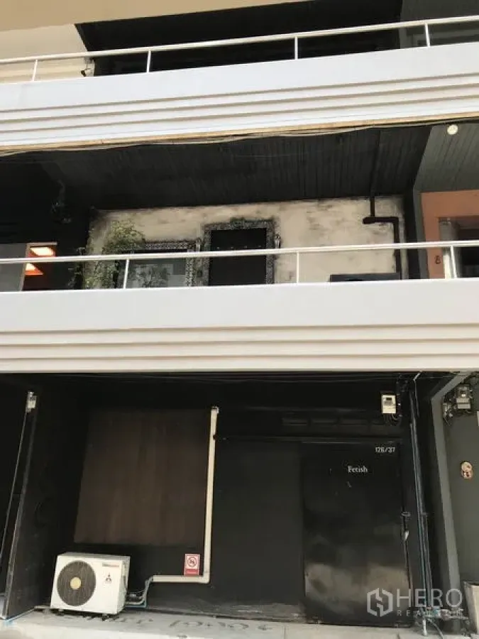 办公空间 出租在Watthana, Bangkok - 艾卡迈瓦他那区低层商业楼外立面，带阳台护栏、可挂招牌的店面与室外空调机组。