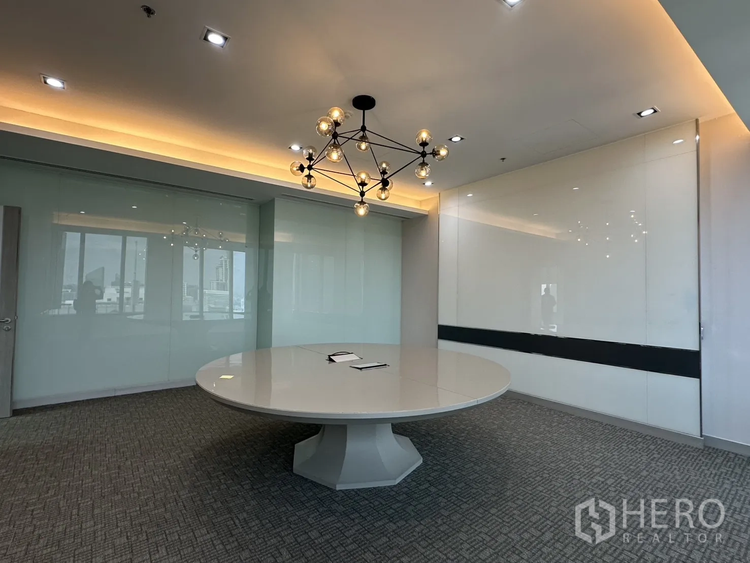 Office Space for rent in Khlong Toei, Bangkok - Modern conference room with a large round table, chandelier, and glass walls.