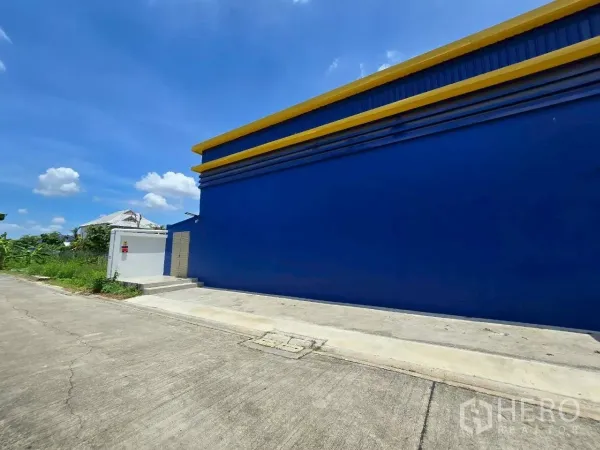 Warehouse for rent or sale in Khlong Toei, Bangkok - Long blue exterior wall of the warehouse along a quiet concrete road.