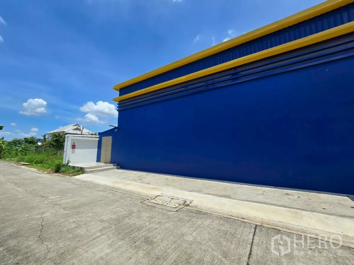 Warehouse for rent or sale in Khlong Toei, Bangkok - Long blue exterior wall of the warehouse along a quiet concrete road.