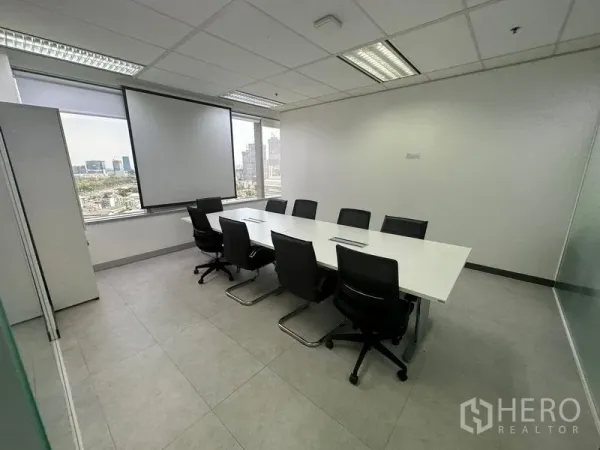 Office Space for rent - Conference room with long white table, black chairs, projector screen and city skyline view.