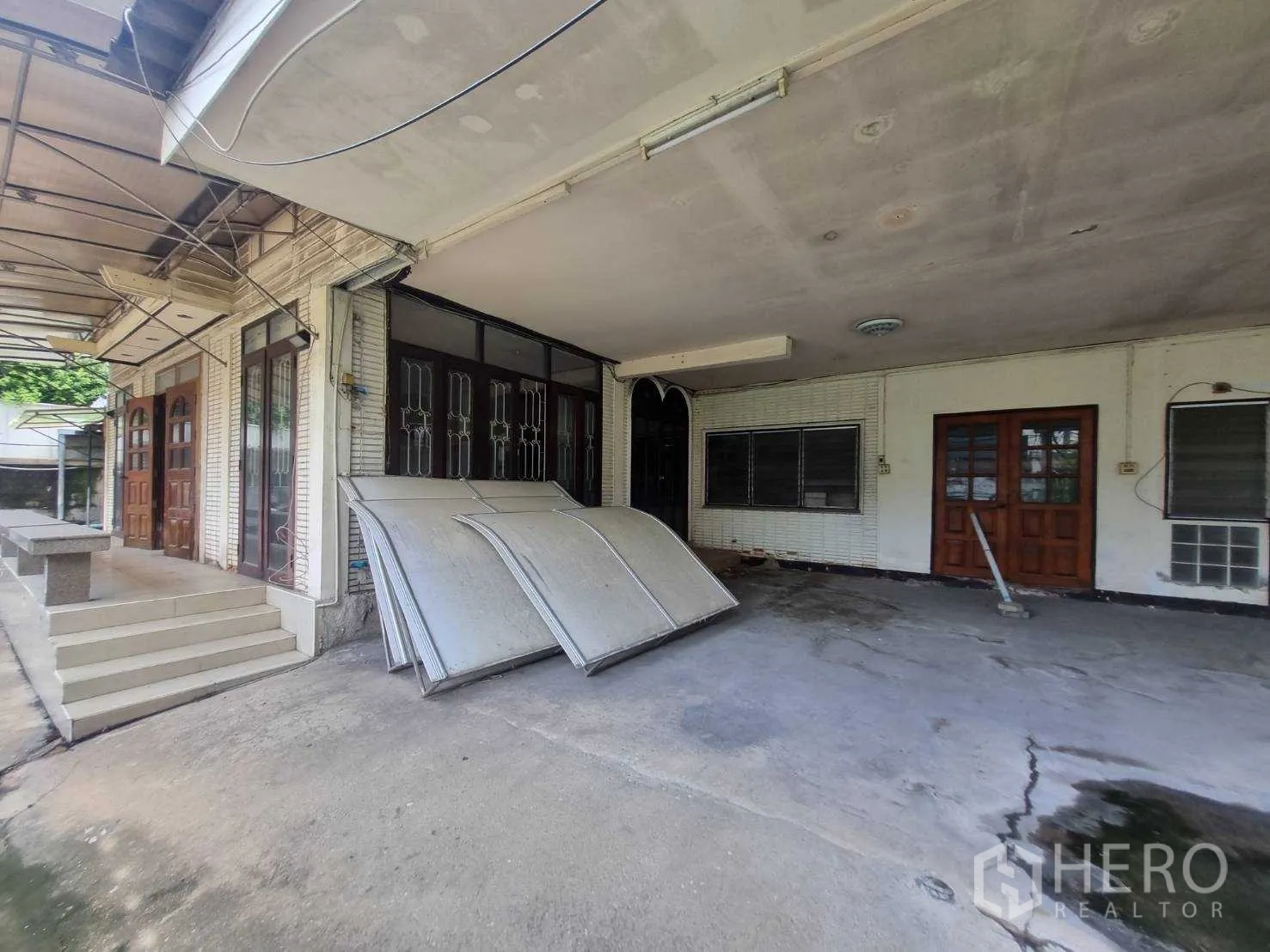 Detached House for rent or sale in Watthana, Bangkok - Covered carport and shaded terrace beside the house with multiple wooden doors.