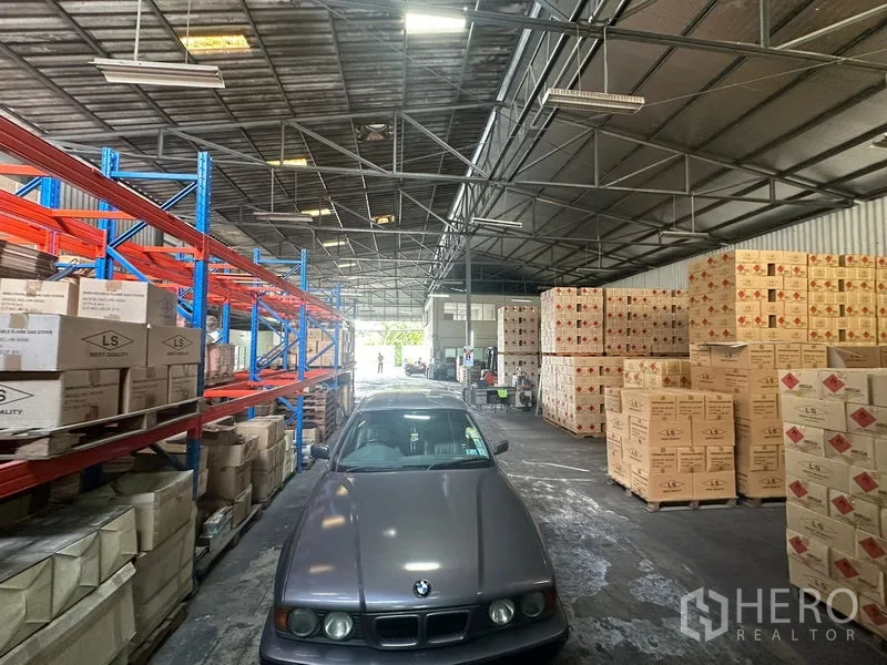 Warehouse for rent in Suan Luang, Bangkok - Aisle with racking system, boxed inventory and a car inside the warehouse.